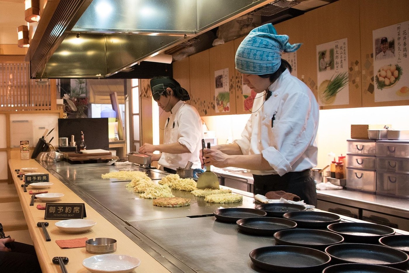 An okonomiyaki on a hotplate, finished with sauce, mayonnaise and green herbs
