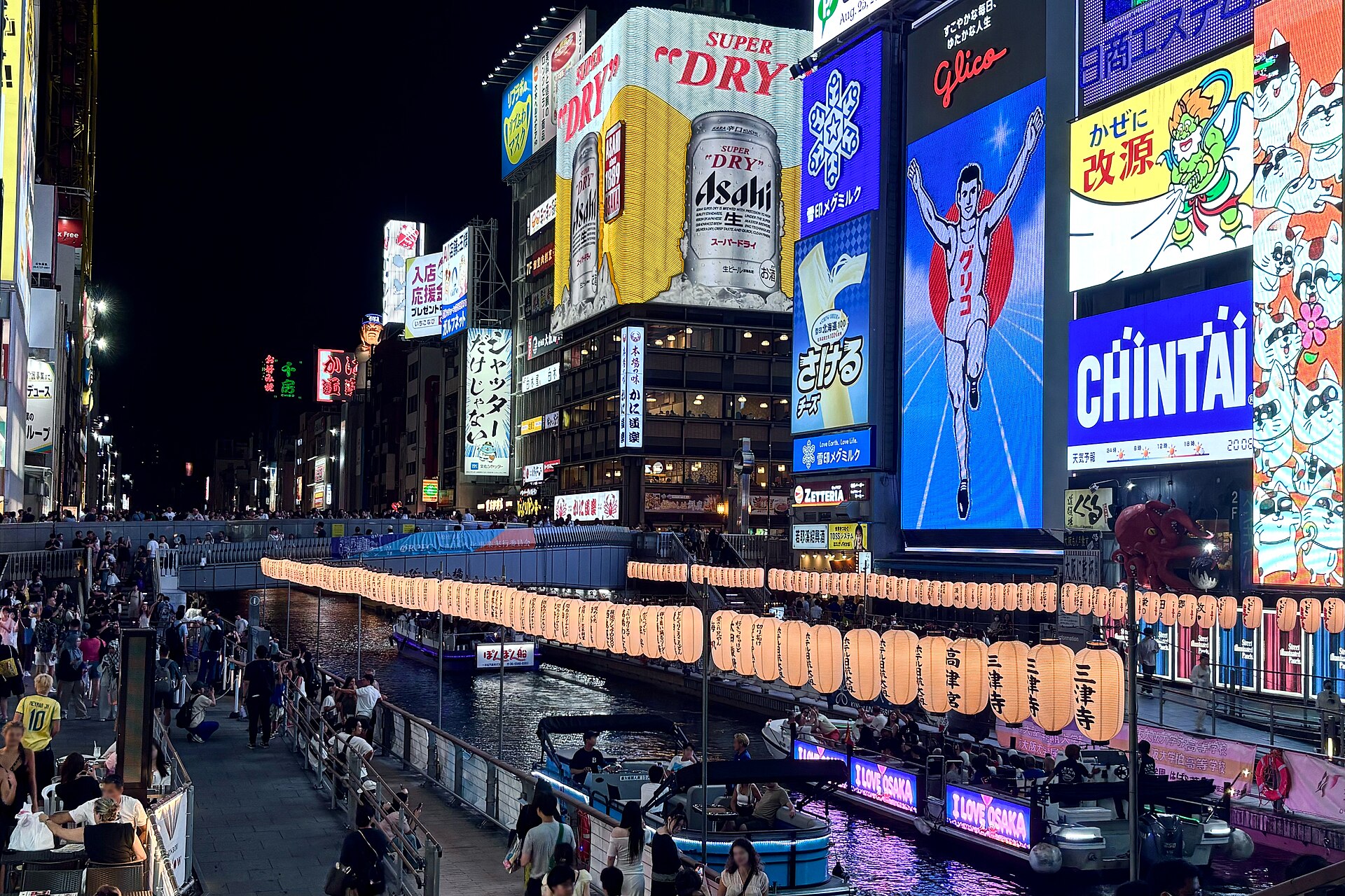 Dotonbori canal at night, neon signs on both banks and a sightseeing boat on the water